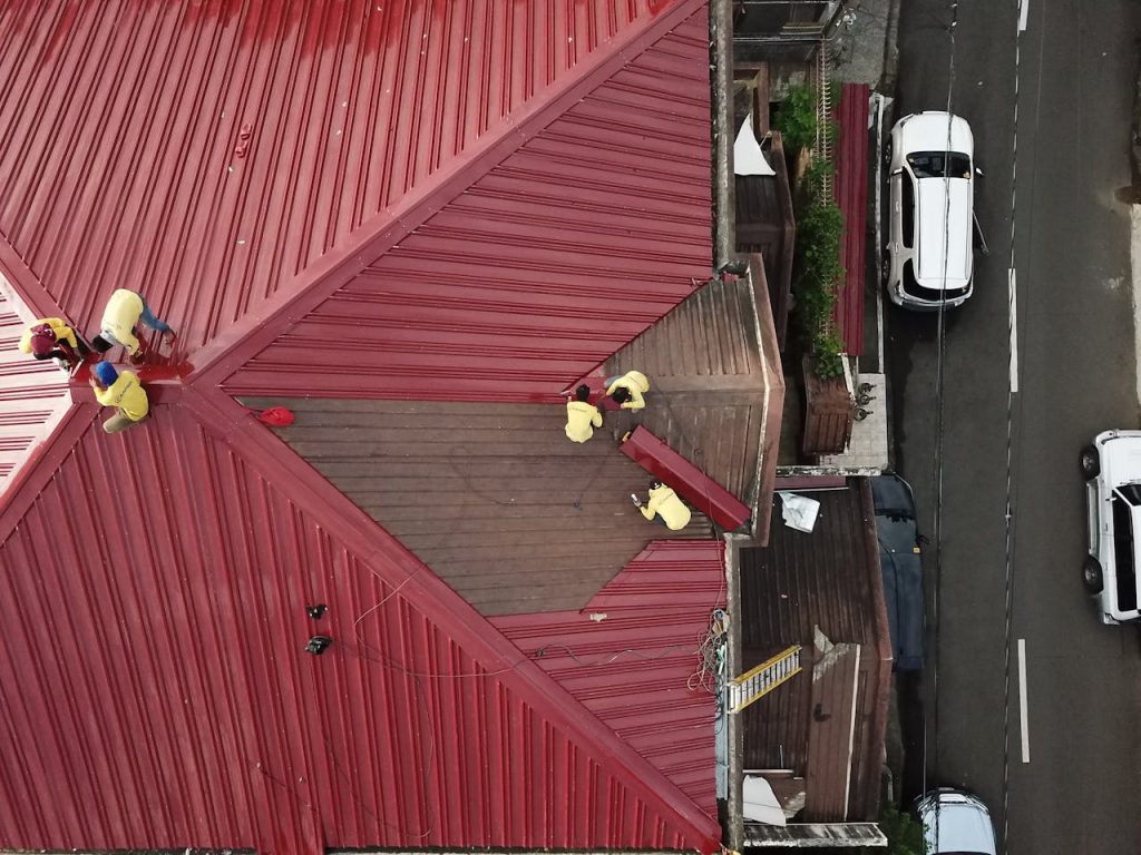 5 Common Roofing Problems and How to Fix Them | TOLAR THINKA LLC Aerial view of workers repairing a red metal roof in Quezon City, Philippines.